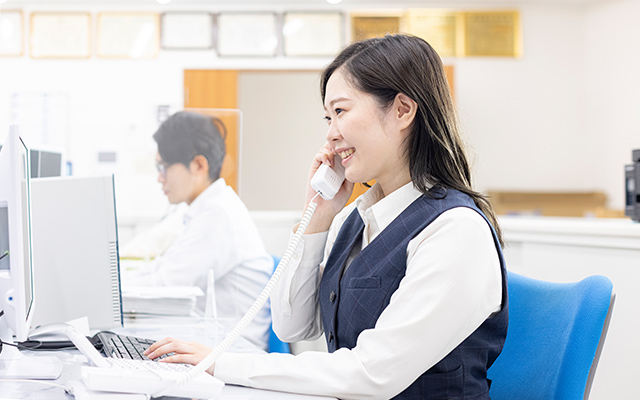 制服を着ている女性社員が机に座り電話している様子